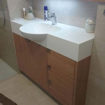 A vanity cabinet for narrow bathrooms with a Corian block countertop and a protruding seamless Corian sink, along with two doors and 3 drawers
