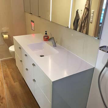Bathroom with a hanging mirrored cabinet above a white vanity cabinet with a seamless Corian sink countertop and 6 drawers