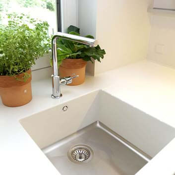 Corian countertop with a seamless Mixa Corian sink with metal bottom and white sides, silver high kitchen faucet, and 2 pots with herbs