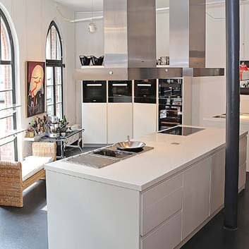 Kitchen studio for group cooking classes with a white minimalist kitchen central island featuring profiled fronts, 2 large range hoods, and professional Miele ovens and cooktops
