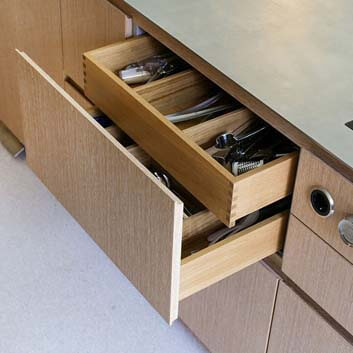 Close-up of an open wooden drawer with cutlery and an inner drawer with visible wood connection, visible Bora control elements.