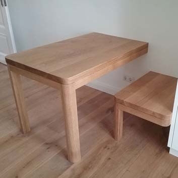 Wooden table with 2 legs, attached to one side of the wall, looks like it's halved by the wall, and a stool with one leg, attached to the wall and one side of the kitchen cabinet, both parts with rounded edges