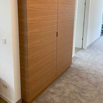 Built-in niche cabinet with continuous wood grain pattern, mitered edges, and recessed handles.