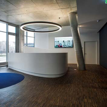 Curved, open elliptical counter made of white Corian with a round LED ceiling light above it.