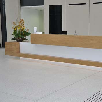 Long office counter made of white Corian with wooden top and decorative shape in front.