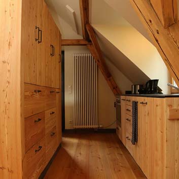 Naturholzküche mit sichtbarer Holzstruktur Berghüttenfeeling mit klobigen schwarzen U-Griffen, Holzboden und Holzschrägbalken