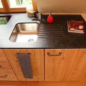 Nahaufnahme der Küche aus Naturholz mit einer schwarz strukturierten, gerillten Corian-Oberfläche und einem nahtlosen Induktionsherd auf der Rückseite der Arbeitsplatte
