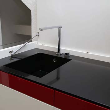 Weiße Küchenzeile mit rotem Streifen auf den Küchenfronten, schwarze Corian-Arbeitsplatte mit nahtloser Corian-Spüle und offener Küchenarmatur mit der Möglichkeit, den oberen Deckel zu schließen, um die Küche zu verbergen und die Einheit wie einen Schrank aussehen zu lassen