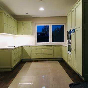 Küche in U-Form mit grünen Rillenfronten und sichtbaren Seiten mit Eckleiste auf den Hängeschränken und Knopfgriffen