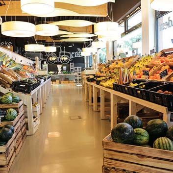 Bio-Supermarkt in Deutschland, hübsche Obst- und Gemüsetheke in Holzkisten und wiederverwendbaren Plastikkisten auf einem maßgefertigten, geneigten Holzdisplay, Deckenlampen aus Holzfurnier