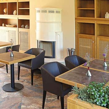 Café mit Wand-zu-Wand-Unterschränken mit Holzfrontrahmen mit Rattaneinlagen und weißen Knöpfen als Zeiger, offene Holzregale über und unter der Decke geschlossene Schränke, quadratische 2-Personen-Tische auf einem Bein und Stühle neben den Tischen