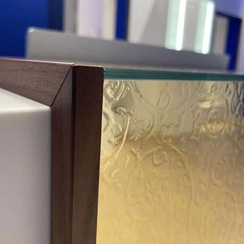 Detailaufnahme einer Corian-Theke mit HPL aus goldmetallischem ABET Laminati mit Nussbaumlamellen an den Seiten und Glas oben
