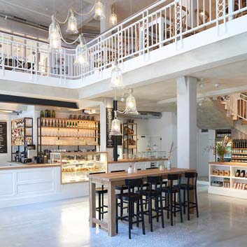 Restaurant in Hamburg, weiße Innenräume, mit offenem Dachboden und Treppe, großer weißer Tresen, der gleichzeitig als Barsitzbereich dient, mit ausgestellten Speisen